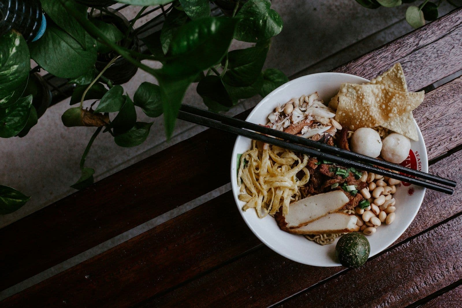 Semangkuk mi dengan irisan daging, bakso, kacang, dan kerupuk pangsit di atas meja kayu