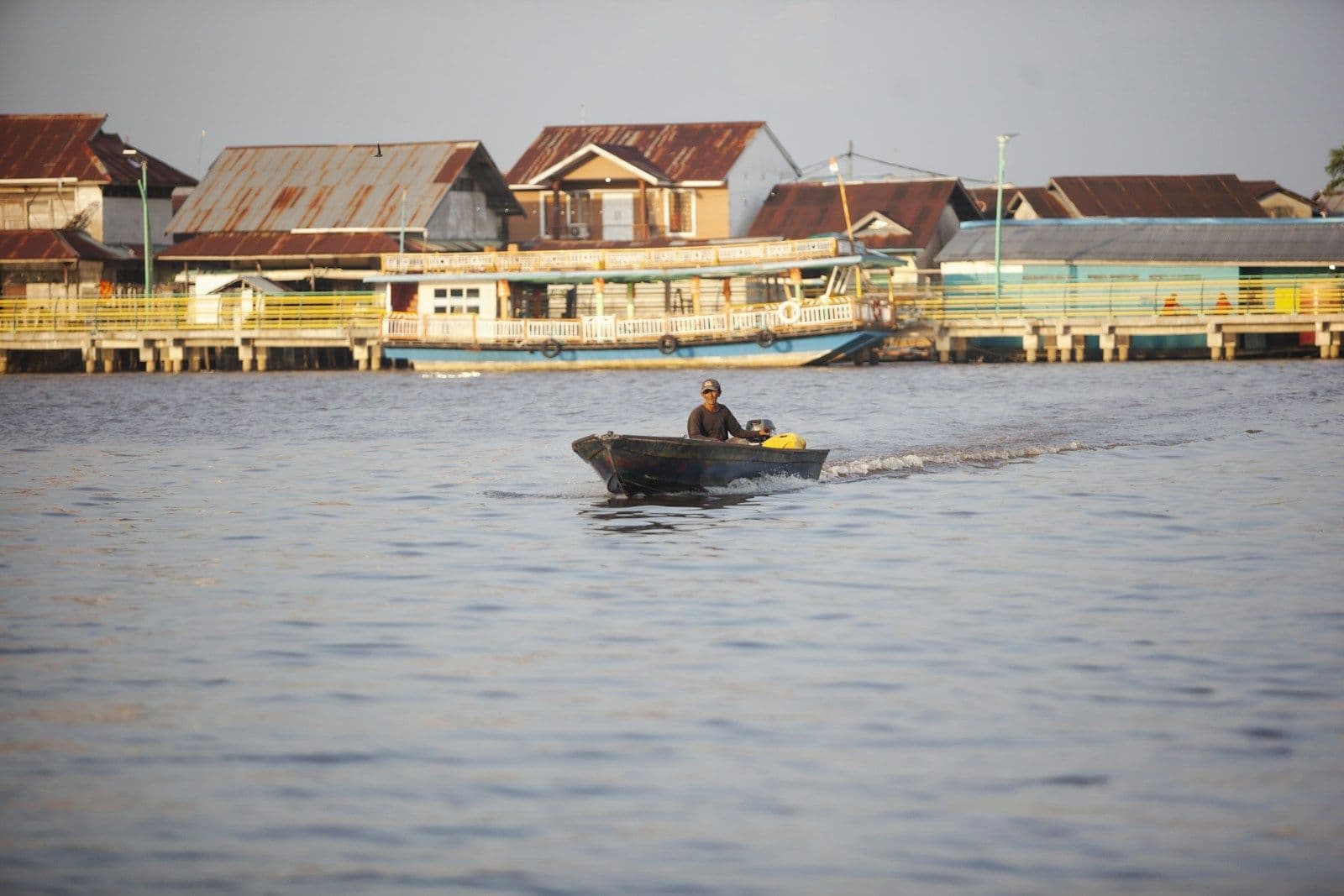Seorang pria mengemudikan perahu kecil di Sungai Kapuas, Pontianak, dengan deretan rumah di tepiannya